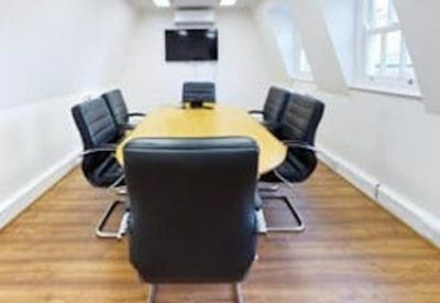 Boardroom with an oval wooden table, black leather chairs, and a wall-mounted TV.