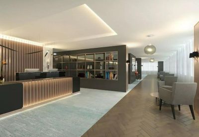 Modern reception area with a wood-slatted desk, soft grey armchairs, and warm lighting.