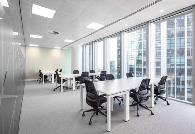 Bright open-plan office with white desks and black ergonomic chairs near floor-to-ceiling windows.
