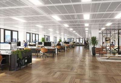 Spacious open-plan office with herringbone wood floors, workstations, and indoor plants.