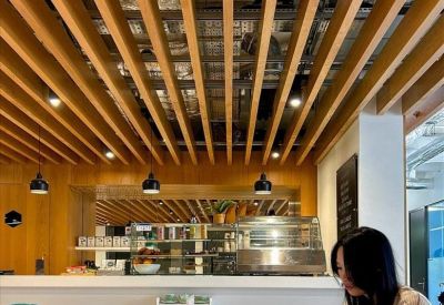Modern coworking cafe with a wooden slat ceiling and a person working on a laptop at a long table.