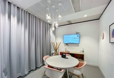Small meeting room with a round table, pink chairs, and a wall-mounted television screen.