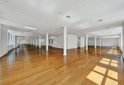 Expansive open-plan office floor with polished wood flooring and white support columns.