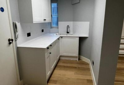Modern office kitchenette with white cabinetry and light wood floors.