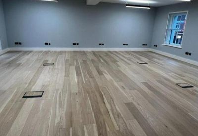 Spacious open-plan office with light wood flooring and grey walls.