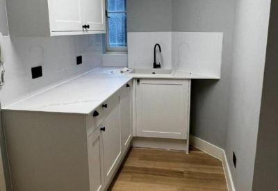 Compact kitchenette area with white cupboards and a black matte faucet.