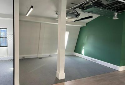Open-plan office space featuring a green accent wall, grey carpeting and exposed ceiling ductwork.