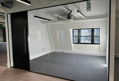Private glass-fronted meeting room with grey carpeting and large industrial-style windows.