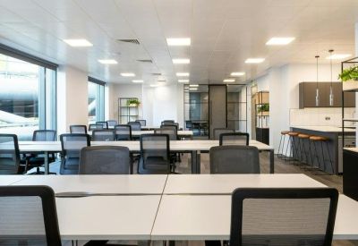 Spacious open-plan office with rows of white desks and ergonomic mesh chairs.