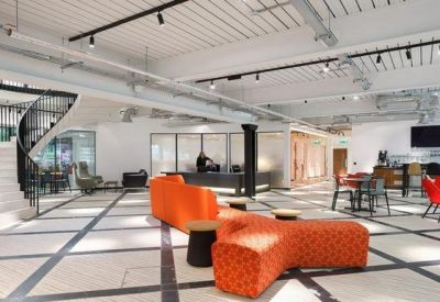 Bright open-plan lobby featuring a curved white staircase and orange modular sofas.