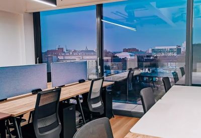 Contemporary office floor with wooden desks, ergonomic chairs, and city views through large windows.