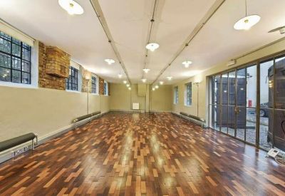 Spacious studio workspace with polished parquet flooring, industrial windows, and warm overhead lighting.