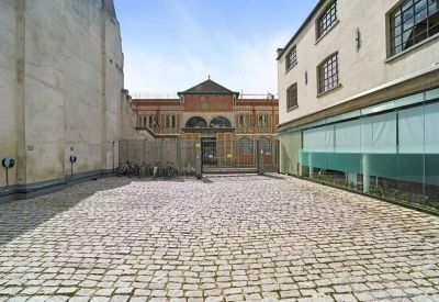 Sunlit cobblestone courtyard surrounded by historic brick and modern glass-fronted buildings.