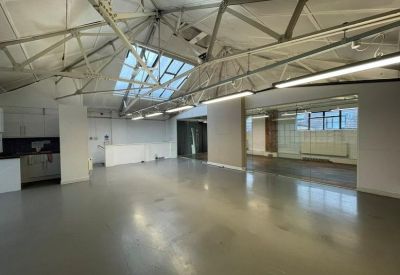 Industrial open-plan workspace with vaulted ceilings, exposed steel trusses, and a large central skylight.