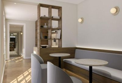 Modern communal area featuring cafe tables, light grey armchairs, and wood-paneled booth seating.