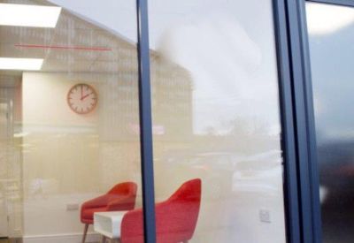 Bright reception seating area with red chairs and a wall clock behind glass.