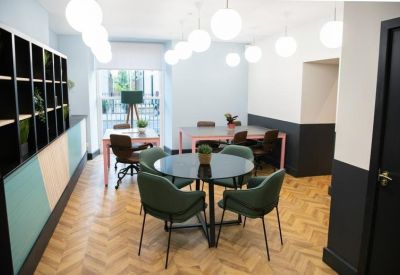 Bright coworking space with round tables, green velvet chairs, and globe pendant lighting.