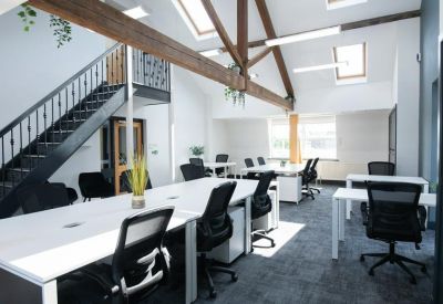 Open-plan office with white desks under high ceilings with exposed wooden beams.