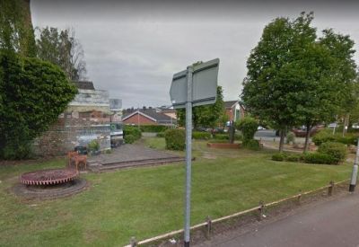 Public green space with a circular brick planter and street signs.