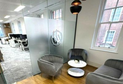Modern communal lounge area with plush grey armchairs and wooden floors next to a glass partition.