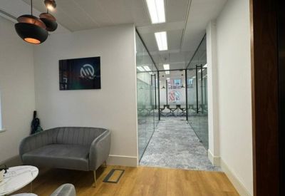 Bright reception waiting area with a comfortable grey sofa and a long glass-walled corridor.