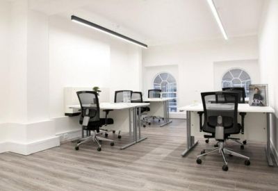 Bright office room with large arched windows and white workstations.
