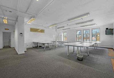 Bright open-plan office space featuring several white communal workstations and grey carpeting.