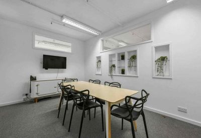 Modern meeting room with a light wood table, black designer chairs, and wall-mounted monitor.