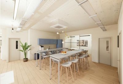 Communal kitchen and dining area with blue cabinetry, long tables, and light wood flooring.