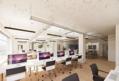 Bright open-plan office space with rows of white desks, purple monitors, and natural light.