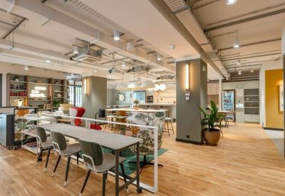 Open-plan coworking space with diverse seating, warm wood floors, and industrial lighting.