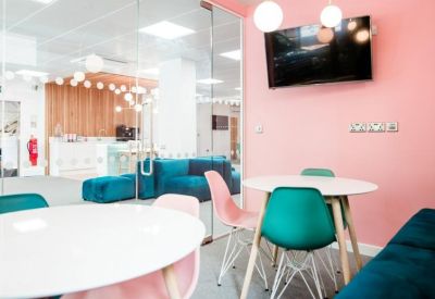 Breakout area with white circular tables and pink and teal chairs against a coral feature wall.