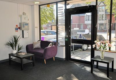 Reception entrance featuring a purple armchair, wooden coffee table, and large glass door.