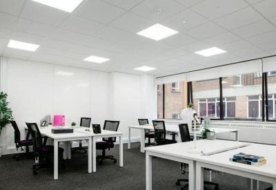 Bright open-plan office with white desks, ergonomic black chairs, and large windows.