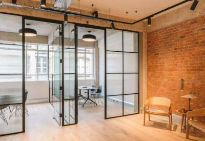 Lounge area featuring an exposed brick wall, glass partitions, and mid-century modern armchairs.