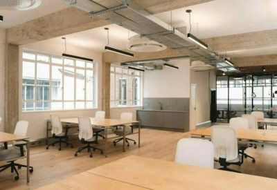 Bright open-plan workspace with wooden floors, exposed beams, and a kitchenette in the background.