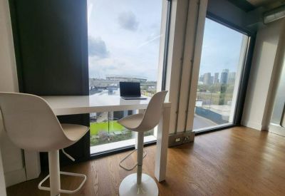 Bright workspace featuring a white desk and bar stools set against a large city-view window.