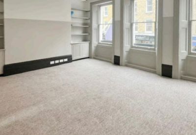 Spacious open-plan office with grey carpet and large windows providing natural light.