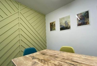 Small office nook with a wooden table, colorful chairs, and green geometric wall paneling.