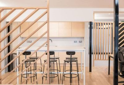 Modern communal kitchen area with light wood cabinets, a white island, and black bar stools.