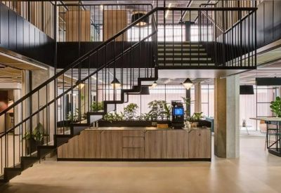 Reception area under a black metal staircase featuring wooden textures and indoor plants.