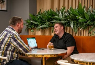 Colleagues laughing at a marble bistro table in a lounge area with wood slat walls and greenery.