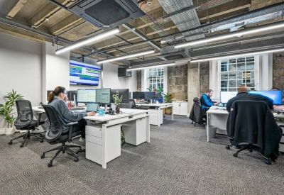 Bright open-plan office with white desks and industrial ceiling details.