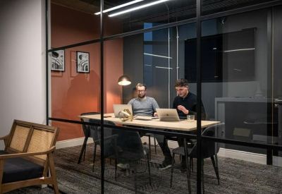 Professional two-person meeting room with laptops and a warm orange feature wall.