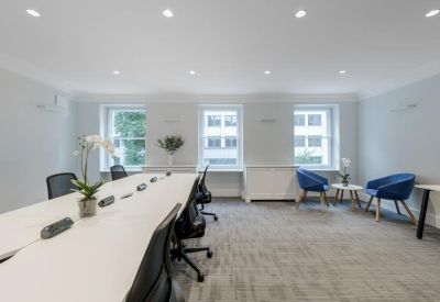 Open-plan office with a long white desk, black ergonomic chairs, and blue lounge seating.