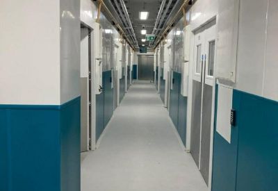 Long industrial-style corridor with teal wall panels and exposed ceiling pipes.
