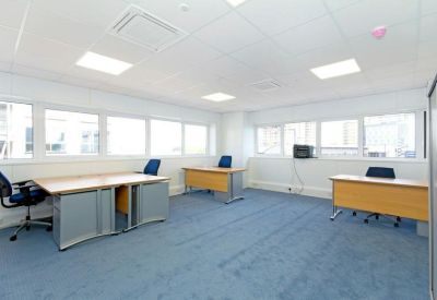 Bright internal office suite with three wooden desks and ergonomic blue chairs.