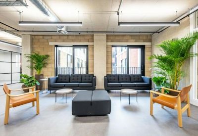 Comfortable lounge area with grey sofas, wooden armchairs, and large indoor plants.