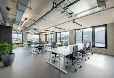 Bright open-plan workspace with white desks, ergonomic chairs, and industrial ceiling details.