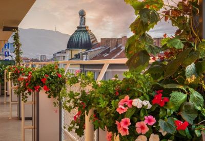 Outdoor balcony terrace with vibrant flower boxes and views of a domed building.